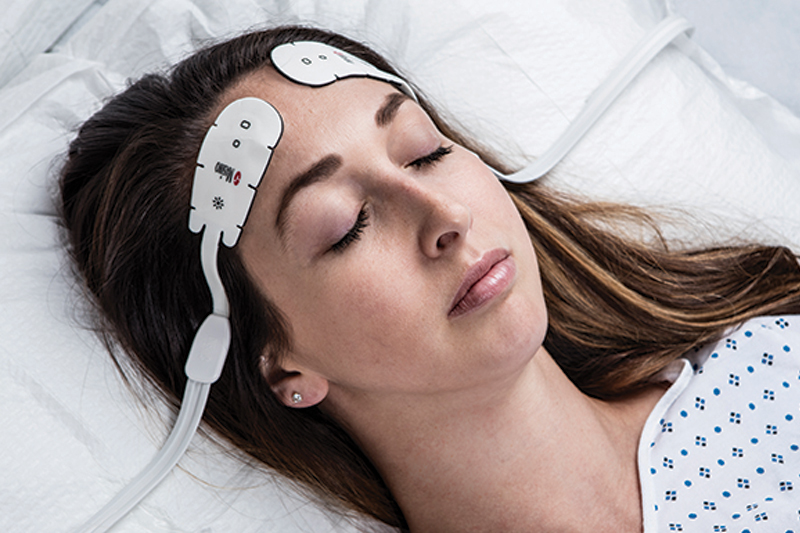 Dark-skinned patient in hospital bed monitored by Masimo Root device.