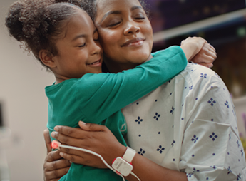 Patient in hospital gown hugging small child.